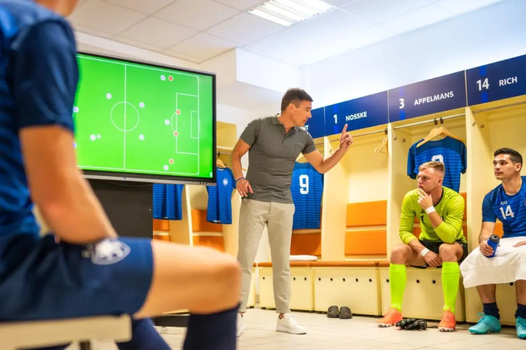 Treinador a orientar jogador em campo equilibrando exigência técnica e apoio